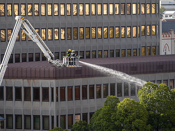 Feuerwehrleute stehen im Rettungskorb einer Drehleiter während der Löscharbeiten am Gebäude des südafrikanischen Parlaments. Foto: Jerome Delay/AP/dpa