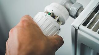 männliche Hand dreht das Thermostat der Heizung auf Null um Strom, Gas und Heizkosten zu Sparen, Hand reguliert Heizkörper