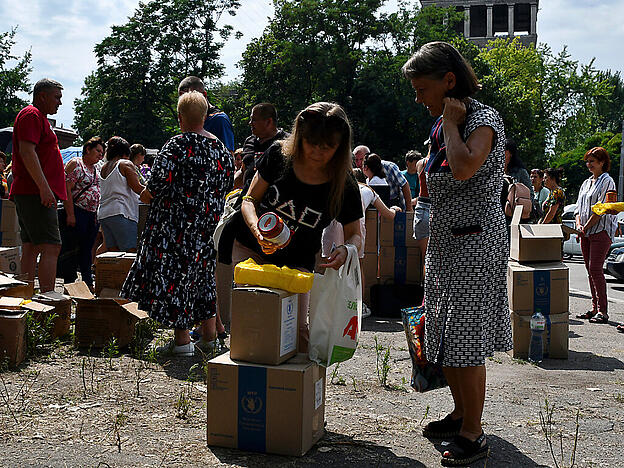 Menschen stehen in einer Schlange, um an einer humanitären Verteilungsstelle Lebensmittel zu erhalten. Foto: Andriy Andriyenko/AP/dpa