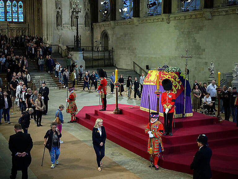 Menschen gehen am Sarg von Königin Elizabeth II. vorbei, der mit der königlichen Standarte, der Imperial State Crown, dem Reichsapfel und dem Zepter des Souveräns geschmückt ist. Foto: Leon Neal/POOL GETTY/AP/dpa