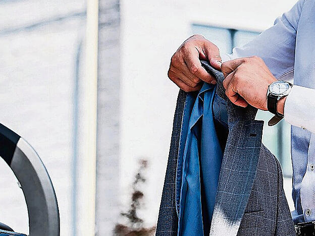 side view of businessman in eyeglasses putting jacket in car trunk at street