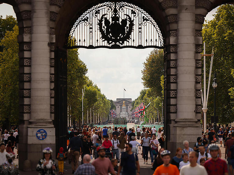 Menschen gehen durch einen Torbogen zur Straße "The Mall" vor dem Buckingham-Palast. Foto: Christian Charisius/dpa